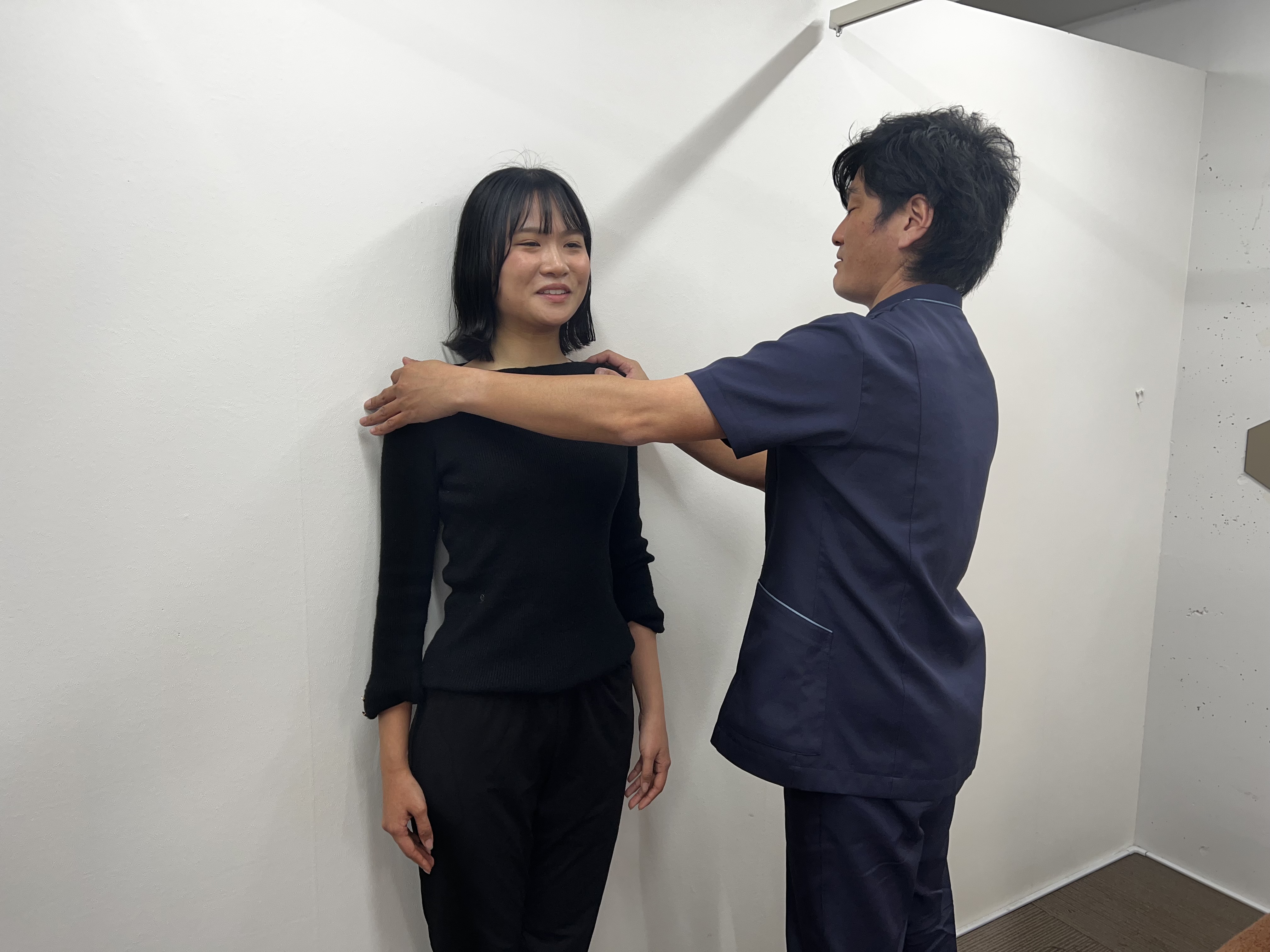 院長が女性customerの肩に触れて検査している、明るい院内での施術風景